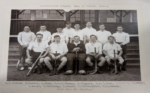 Black and white photo of the 1943-44 hockey team, standing and sitting with hockey sticks, outside the Pavillion